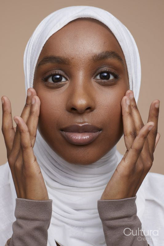 Studio portrait of young woman in white hijab touching face