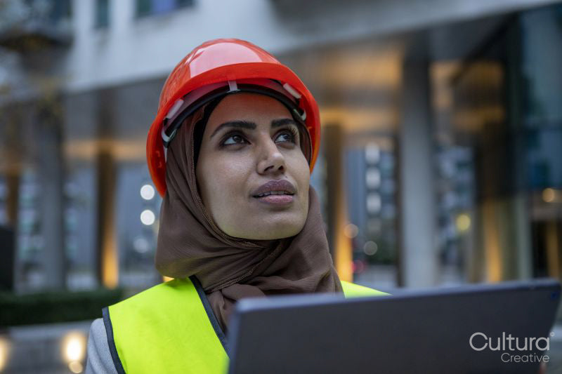 Female engineer in hijab and hardhat using digital tablet
