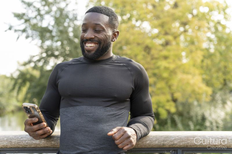 Smiling athletic man looking at smart phone on footbridge in park