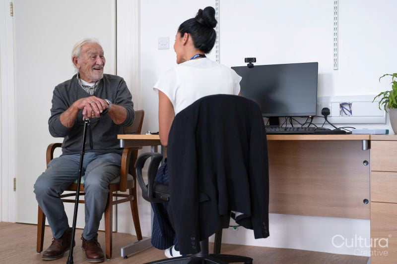 Smiling senior patient talking to female doctor at desk in office