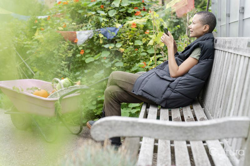Smiling woman with smart phone in vegetable garden