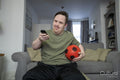 Man sitting on sofa, holding soccer ball and remote control