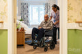 Female care giver pushing senior man in wheelchair in nursing home