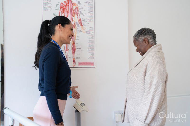 Smiling female therapist assisting senior woman standing on weight scale