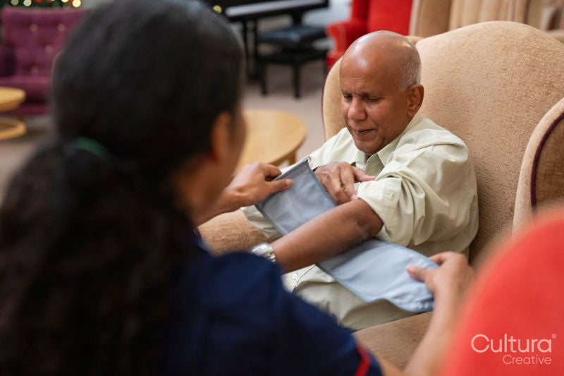 Nursing assistant adjusting blood pressure gauge on senior mans arm in nursing home