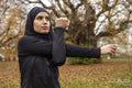 Woman in black sports clothing and hijab stretching in park