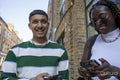 Smiling woman and man using smart phone on street