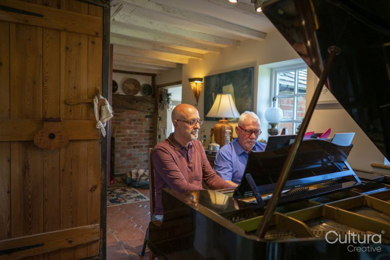 Senior male couple playing piano at home