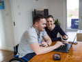 Smiling man on wheelchair and woman looking at laptop at home