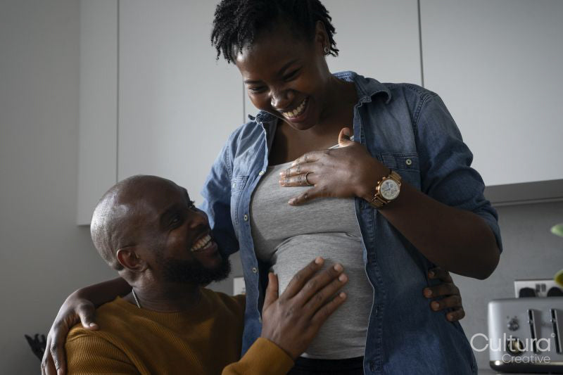 Smiling man touching pregnant woman's belly in kitchen