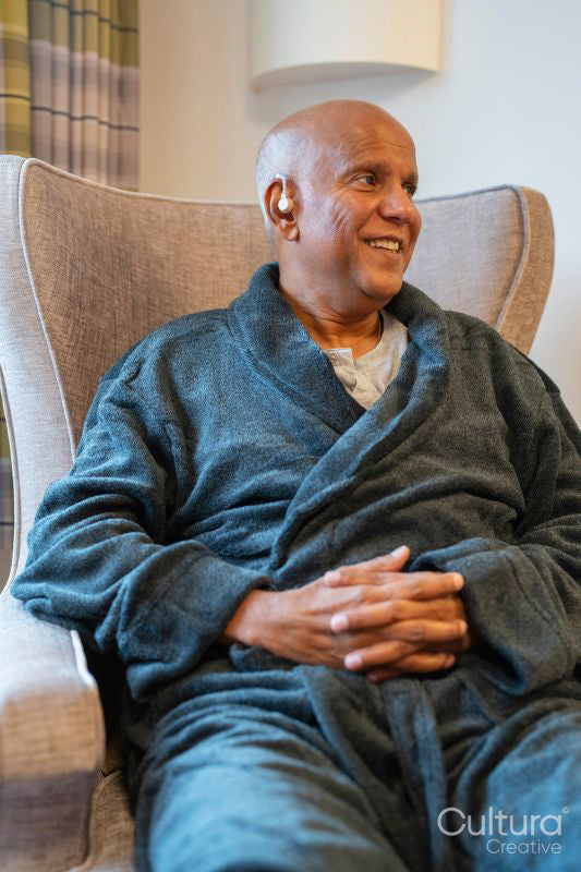 Senior man sitting in armchair with hearing aid in his room at nursing home