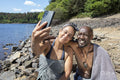 Smiling couple wrapped in towels taking selfie on lakeshore, Yorkshire, UK