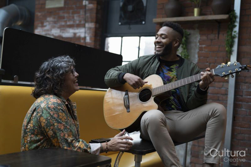 Young man playing acoustic guitar in office lounge, woman laughing