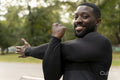 Portrait of smiling athletic man stretching arm in park