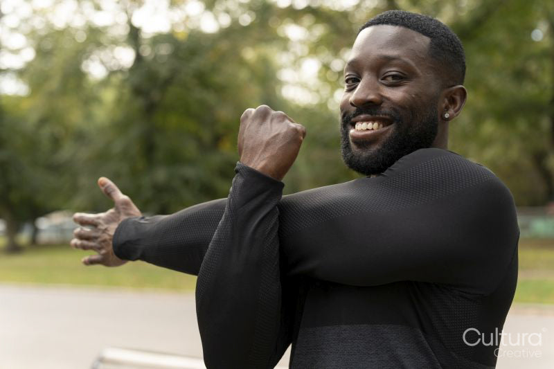 Portrait of smiling athletic man stretching arm in park