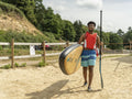 Young man carrying paddleboard and oar on beach