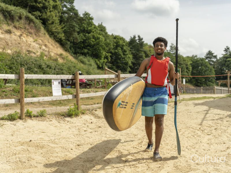 Young man carrying paddleboard and oar on beach