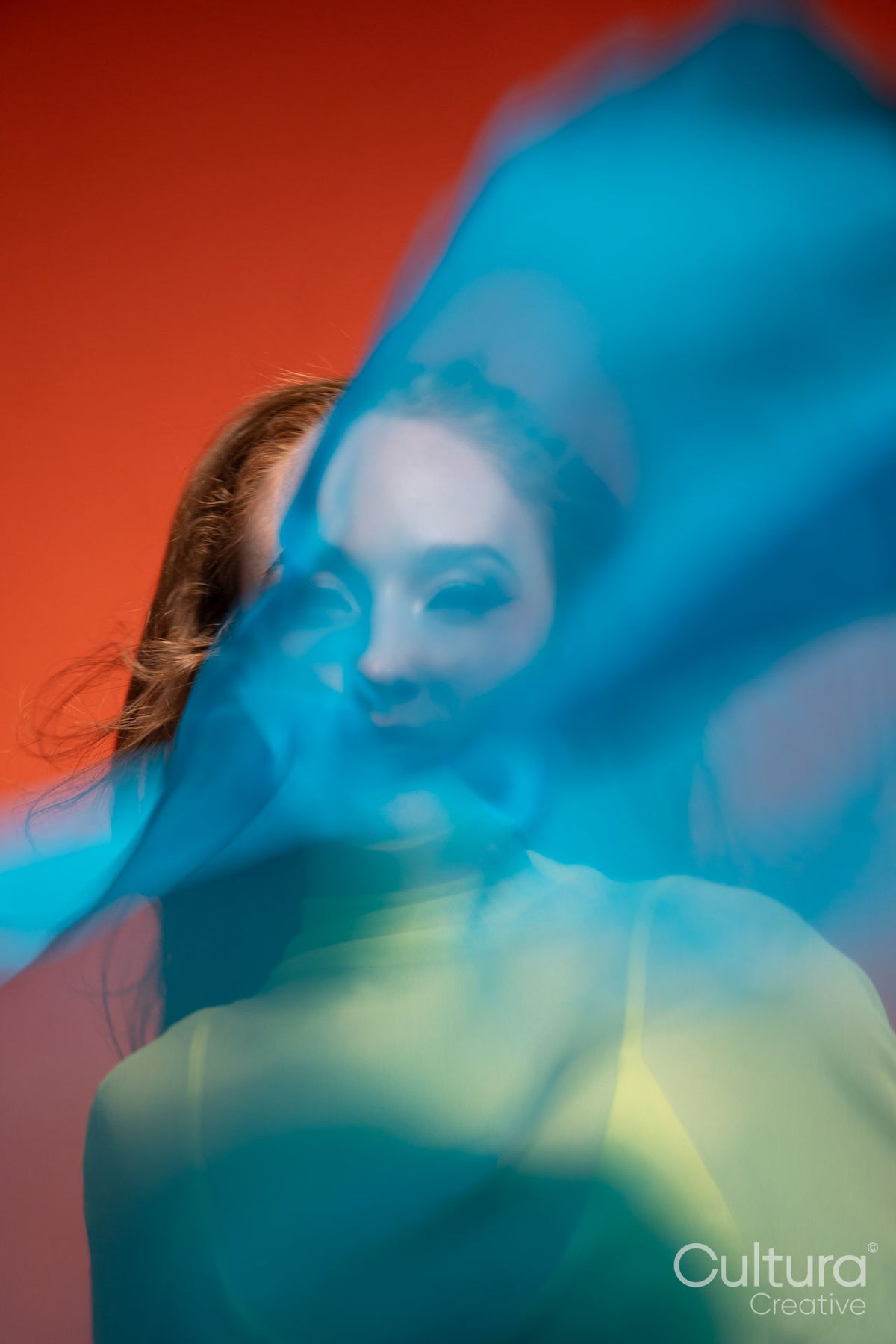 Woman in yellow dress veiled by flowing blue sheer fabric