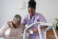 Caregiver assisting smiling senior woman sitting on bed