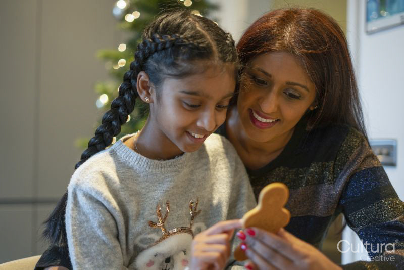 Smiling mother and daughter looking at homemade gingerbread man in kitchen