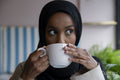 Young woman in hijab drinking coffee in cafe