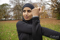 Woman in black sports clothing and hijab stretching in park