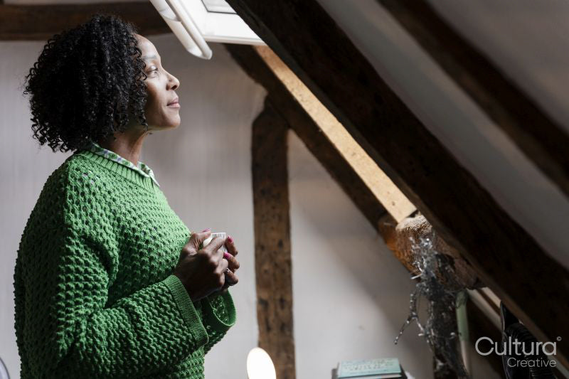 Thoughtful woman holding cup of coffee while looking through window