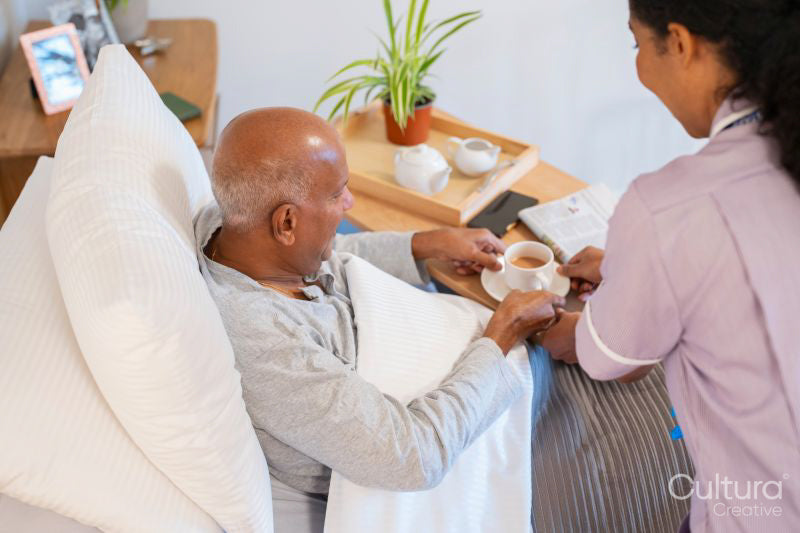 Nurse serving coffee to senior man lying in bed in room at nursing home