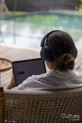 Rear view of woman using laptop with headphones at poolside