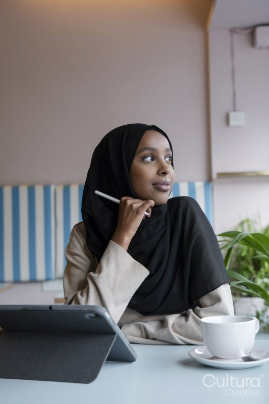 Young woman in hijab working on tablet in cafe