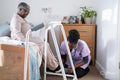 Caregiver helping senior woman sitting on bed to put on slippers