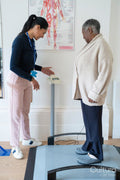 Smiling female therapist assisting senior woman standing on weight scale