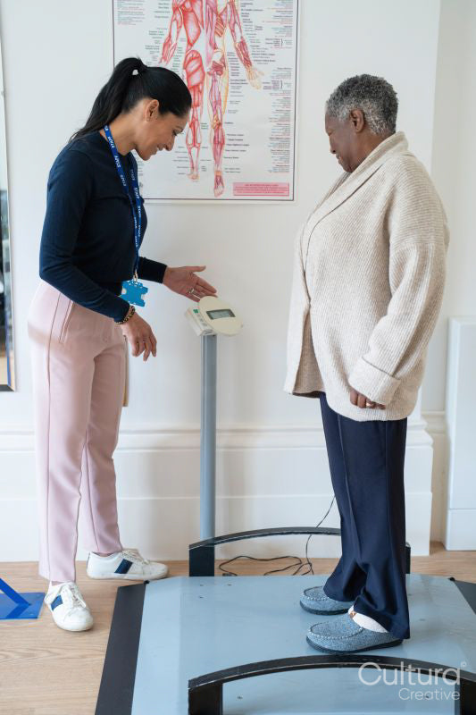 Smiling female therapist assisting senior woman standing on weight scale