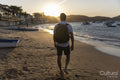 Rear view of man with backpack on beach at sunset