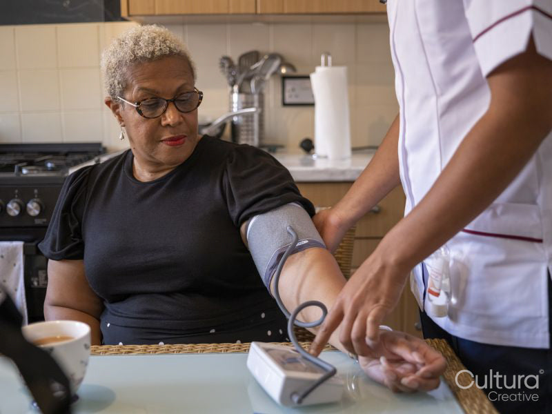 Nurse visiting mature woman at her house, measuring blood pressure