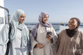 Three Muslim women laughing while standing on pier on sunny day