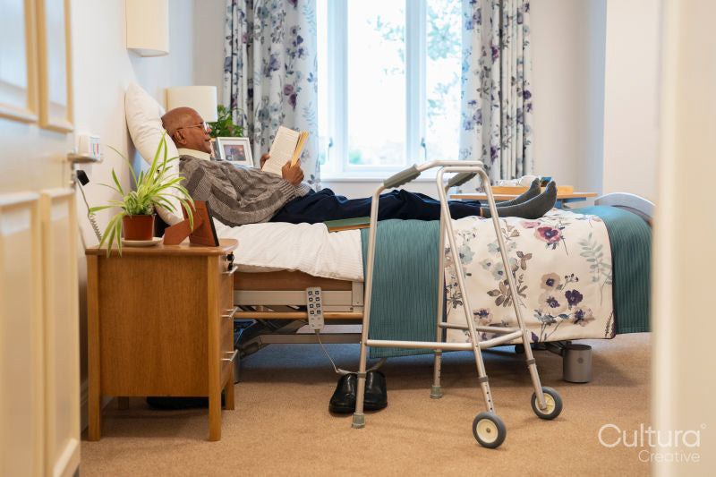 Senior man reading book while lying on bed in his room at nursing home
