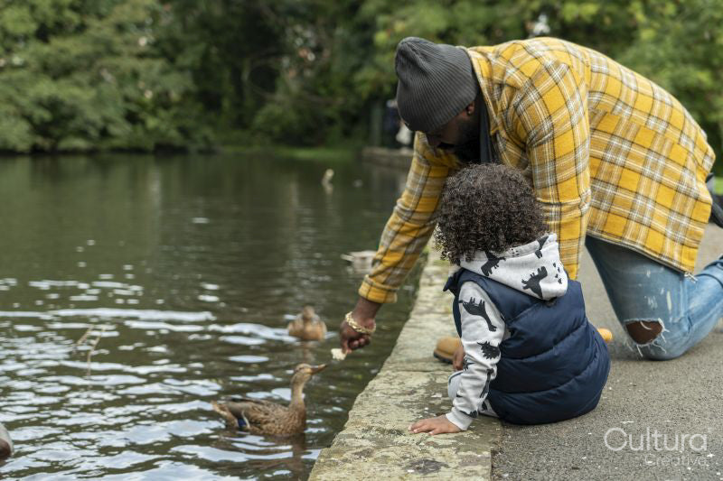 Father with daughter feeding duck on pond in park