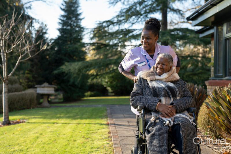 Nurse and senior woman in wheelchair going on walk in park