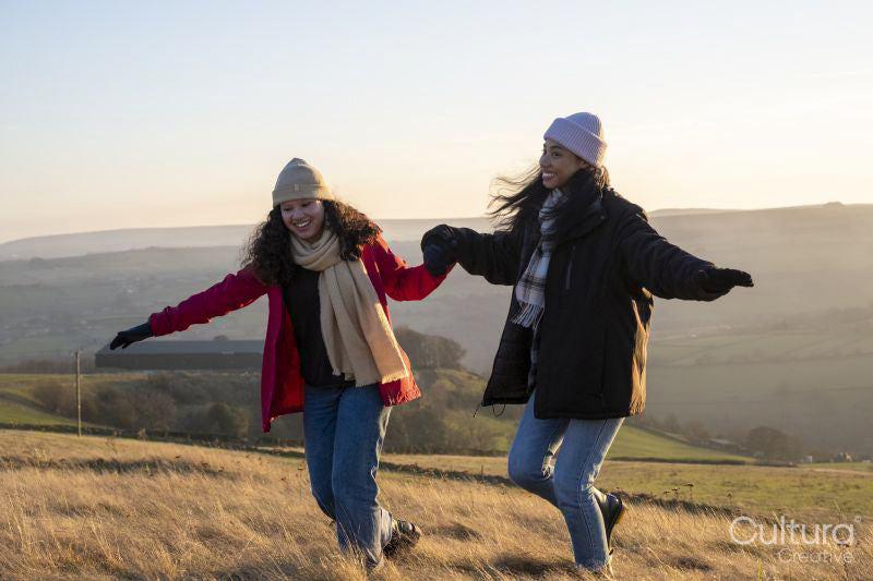 Smiling female friends hiking in rural landscape and holding hands