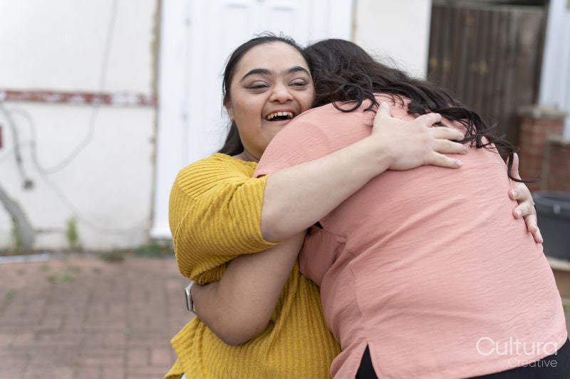 Woman embracing down syndrome daughter in front of house
