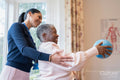 Smiling female therapist assisting senior woman exercising with ball