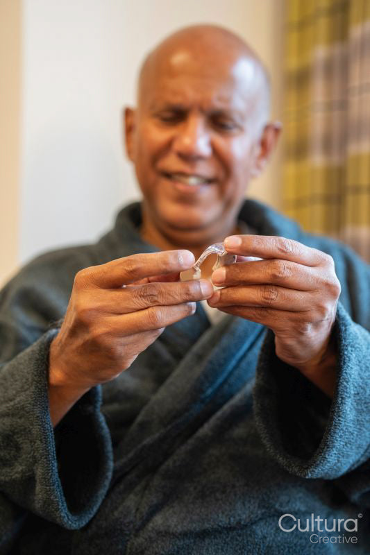 Senior man holding hearing aid in his room at nursing home