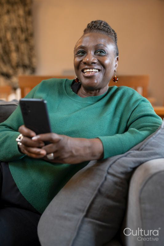 Smiling senior woman relaxing on sofa and using phone