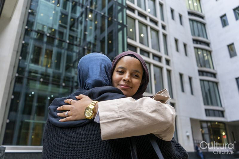 Two women wearing hijabs hugging in street