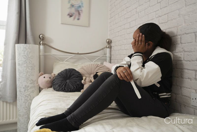 Girl sitting on bed with pregnancy test