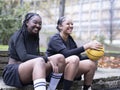Two female friends sitting outdoors with basketball