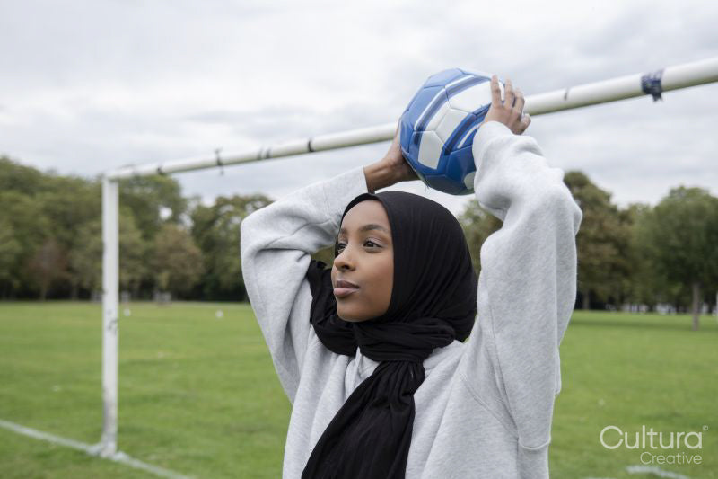 Smiling woman in hijab throwing soccer ball in park