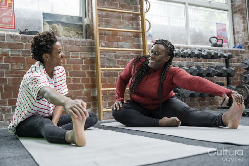 Mother and daughter stretching on mat in gym