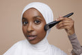Studio portrait of young woman in white hijab applying make-up